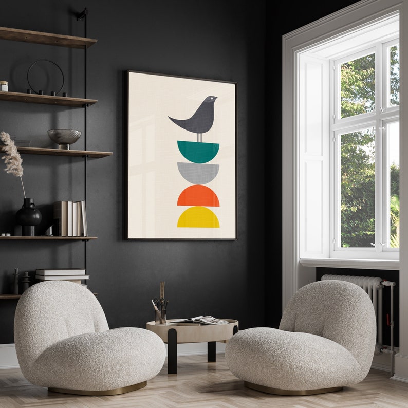 May include: A framed wall art print featuring a dark gray bird perched atop a vertical stack of four semi-circles in teal, gray, orange, and yellow, set against a cream background. The artwork is displayed in a black frame on a dark wall.
