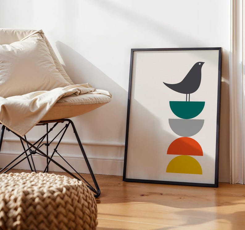 May include: A framed vertical wall art print featuring a dark gray bird perched atop a vertical stack of four semi-circles in teal, gray, orange, and yellow colors. The artwork is set against a light cream background within a thin black frame.