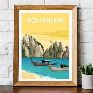 May include: A framed art print featuring a scenic illustration of Koh Phi Phi, Thailand. The artwork depicts a yellow sky, turquoise water, limestone cliffs, and traditional longtail boats. The text "KOH PHI PHI" is at the top.