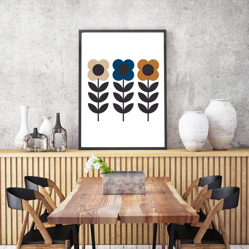 Op de afbeelding: Een ingelijst afdruk van drie gestileerde bloemen met zwarte stelen en bladeren. De bloemen zijn beige, blauw en oranje.
