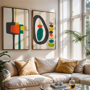 May include: Two rectangular wall art prints in wooden frames featuring abstract geometric shapes. The left print displays dark gray, orange, yellow, and teal forms. The right print shows a large dark gray oval with teal and orange shapes inside, plus a vertical stack of multicolored pebbles.