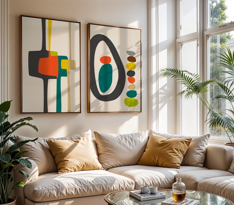 May include: Two rectangular wall art prints in wooden frames featuring abstract geometric shapes. The left print displays dark gray, orange, yellow, and teal forms. The right print shows a large dark gray oval with teal and orange shapes inside, plus a vertical stack of multicolored pebbles.
