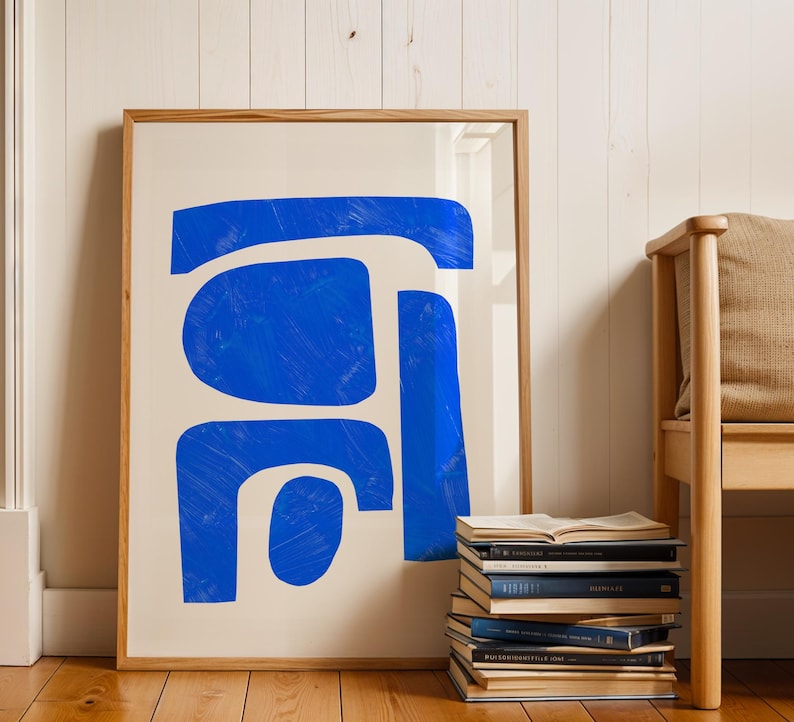 May include: A framed wall art print featuring a series of bold, abstract blue shapes with visible brushstroke textures against a solid off-white background. The artwork is enclosed in a light-toned wooden frame with a clean, simple profile.