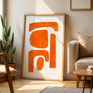 May include: A framed vertical wall art piece featuring abstract orange shapes with visible brushstroke textures on a white background. The artwork is enclosed in a light-toned wooden frame, displaying a series of organic, rounded forms.