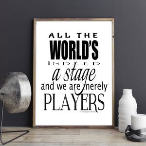 May include: A framed print with the quote "All the world's a stage and we are merely players" in black text. The print is in a wooden frame and is displayed on a wooden surface with decorative items.