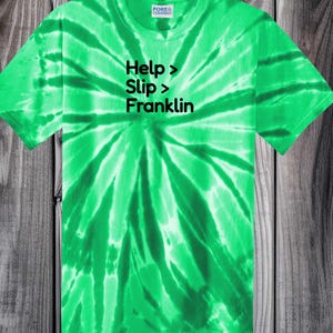 May include: A bright green tie-dye t-shirt with the text "Help > Slip > Franklin" in black. The shirt is a crew neck style and features the Port & Company logo on the tag.