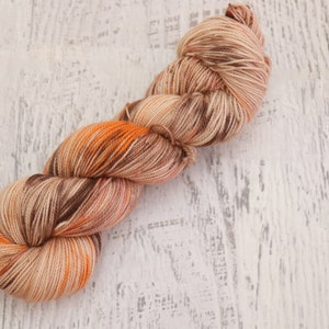 May include: A skein of yarn in shades of brown, orange, and beige. The yarn is arranged in a loose coil.