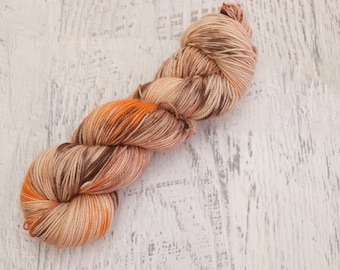 May include: A skein of yarn in shades of brown, orange, and beige. The yarn is arranged in a loose coil.