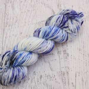 May include: A skein of yarn in shades of white, blue, and purple. The yarn is hand-dyed and has a speckled appearance.