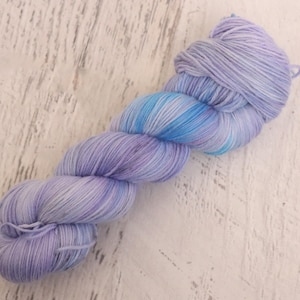 May include: A skein of hand-dyed yarn in shades of lavender, light blue, and white. The yarn is arranged in a twisted, elongated shape, with the colors blending together. The yarn is likely made of a soft fiber, perfect for knitting or crocheting projects.