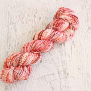 May include: A skein of yarn in a red, white, and orange colorway. The yarn is twisted and has a speckled appearance.