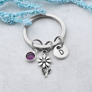 May include: A silver key chain with a purple gemstone, a silver daisy charm, and a silver charm with the letter "D" on it.