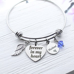 May include: A silver bangle bracelet with a heart charm that says "forever in my heart", a wing charm, a round charm that says "Husband" with a heart, and a blue crystal charm.