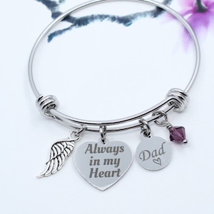 May include: Silver bangle bracelet with a heart charm engraved with "Always in my Heart", a small round charm engraved with "Dad" and a small purple crystal charm. The bracelet also has a silver wing charm.