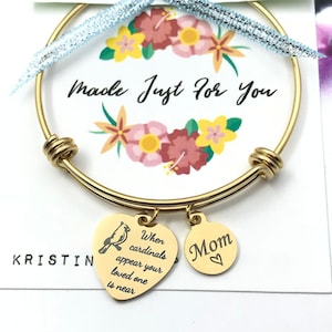 May include: Gold expandable bracelet with two charms. One charm is a heart with the word "Mom" and a heart symbol. The other charm is a heart with a cardinal bird and the text "When cardinals appear your loved one is near".