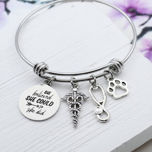 May include: Silver charm bracelet with a paw print, stethoscope, medical symbol, and a round charm with the text "She believed she could so she did".