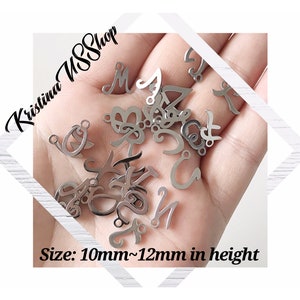 May include: A close-up of a hand holding a variety of silver metal letter charms. The charms are approximately 10mm to 12mm in height. The text "Kristina SSShop" is visible in the background.