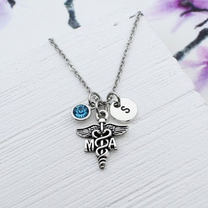 May include: Silver necklace with a medical caduceus charm, a blue crystal, and a personalized disc with the letter 'S'.