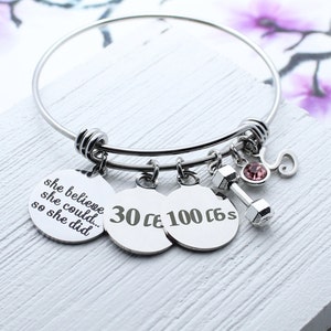 May include: Silver charm bracelet with a dumbbell charm, a pink rhinestone, and three round charms with the text "she believe she could... so she did", "30", and "100 6s".