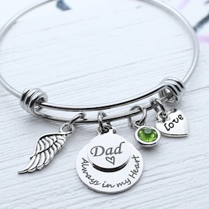 May include: Silver bangle bracelet with charms. The charms include a wing, a round charm with the text "Dad Always in my Heart" and a heart charm with the text "Love".