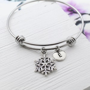 以下が含まれることがあります： 雪の結晶のチャームとEの文字の小さなチャームが付いたシルバーのバングルブレスレットです。