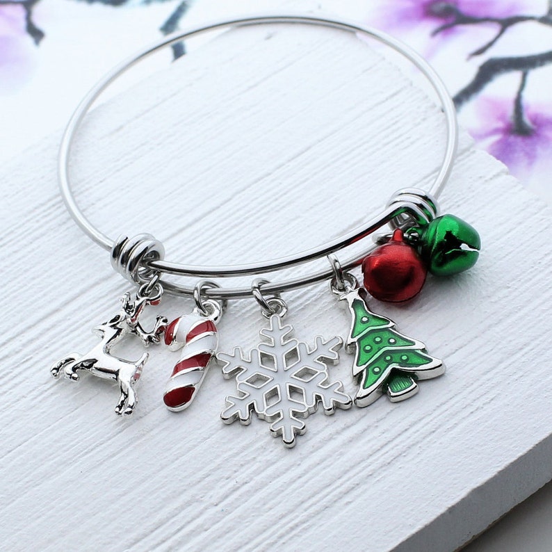 Puede incluir: Un brazalete de plata con abalorios, entre los que se incluyen una ca&ntilde;a de az&uacute;car roja y blanca, un &aacute;rbol de Navidad verde, una bola roja, un copo de nieve plateado y un reno plateado.