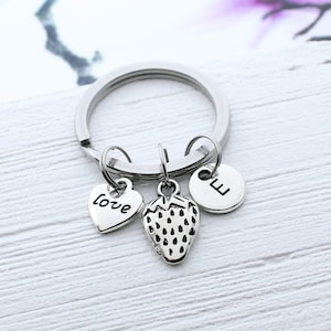 May include: Silver keychain with a heart charm that says "love", a strawberry charm, and a round charm with the letter "E".