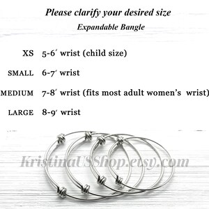 May include: Four expandable silver bangles in different sizes. The sizes are labeled as XS, Small, Medium, and Large. The sizes correspond to wrist sizes of 5-6 inches, 6-7 inches, 7-8 inches, and 8-9 inches. The bangles are on a white wooden surface.