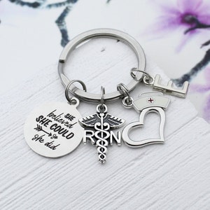 May include: Silver keychain with a round charm that says "She believed she could so she did" with an arrow pointing to the right. The keychain also has a charm with a medical caduceus and the letters "RN" and a heart charm. There is also a small charm with the letter "E".