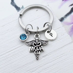 May include: Silver keychain with a medical caduceus charm, a blue crystal charm, and a charm with the letter "P".
