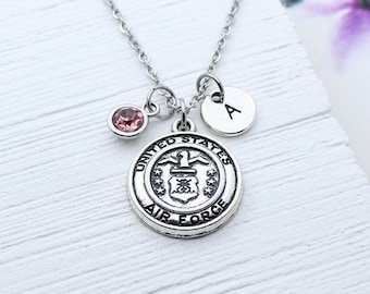 May include: A silver necklace with a charm featuring the United States Air Force emblem, a pink crystal charm, and a silver charm with the letter "A".