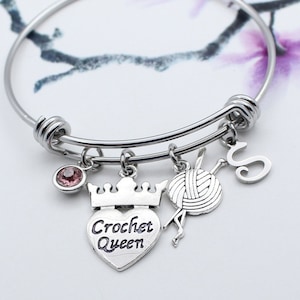 May include: Silver bangle bracelet with charms including a heart with the text "Crochet Queen", a crown, a ball of yarn, a crochet hook, and a letter "S".