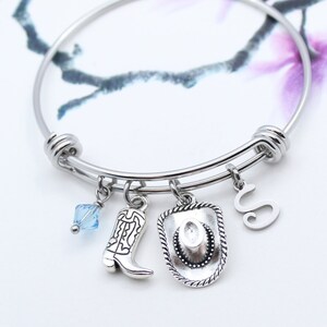 May include: A silver charm bracelet with a blue crystal charm, a cowboy boot charm, a cowboy hat charm, and a letter "S" charm.