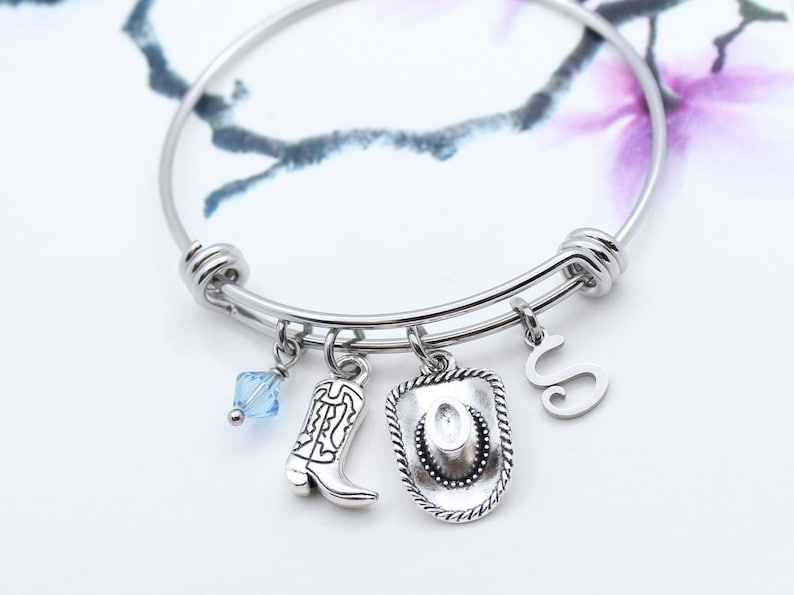 May include: A silver charm bracelet with a blue crystal charm, a cowboy boot charm, a cowboy hat charm, and a letter "S" charm.