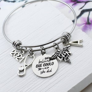 May include: A silver charm bracelet with a stethoscope, a charm that says "She believed she could so she did", a charm with the letters "LPN" and a caduceus, a charm with the year 2021, and a charm with the letter "A".