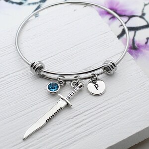 May include: A silver bangle bracelet with a blue crystal charm, a knife charm, and a charm with the letter "P" on it.