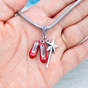 May include: Silver charm bracelet with a red ruby slipper charm and a silver star wand charm.