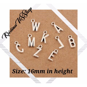 May include: Silver-colored metal alphabet charms, including letters W, M, K, L, B, A, C, Z, and E, are displayed on a brown card. The charms are approximately 16mm in height. The shop name "Kristina USShop" is in the upper left corner.