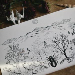 May include: Black and white illustration of a landscape with mountains, trees, and a bee. A small tower is visible in the distance. The artwork is on a white paper, with dried flowers and a small bone-like object in the background.