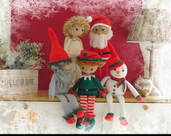 May include: A group of five crocheted Christmas decorations, including a Father Christmas, a snowman, a gnome, an elf, and an angel. The decorations are sitting on a shelf with a wooden sign that reads "Live Laugh Love".