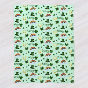 May include: A green and white baby blanket with a repeating pattern of shamrocks, rainbows, leprechaun hats, and gold horseshoes. The name "Bailey" is repeated throughout the pattern.