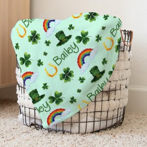 May include: A green fleece blanket with a repeating pattern of shamrocks, rainbows, gold horseshoes, and leprechaun hats. The blanket is personalised with the name "Bailey".