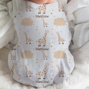 May include: White baby sleeper with a pattern of brown giraffes, gold stars, and beige clouds. The sleeper has the name "Matthew" printed three times on the front.