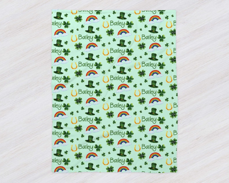 May include: A green and white baby blanket with a repeating pattern of shamrocks, rainbows, leprechaun hats, and gold horseshoes. The name "Bailey" is repeated throughout the pattern.