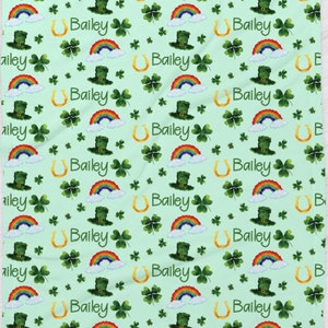 May include: A green and white fabric with a repeating pattern of rainbows, shamrocks, horseshoes, and leprechaun hats. The name Bailey is repeated throughout the pattern.