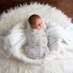 May include: A white swaddle with a giraffe and star pattern. The swaddle is personalized with the name "Matthew".
