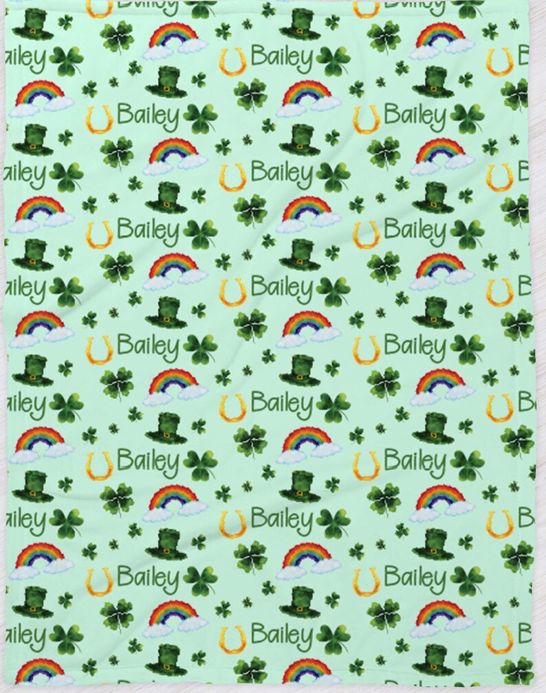 May include: A green and white patterned baby blanket with a rainbow, shamrock, and horseshoe design. The name "Bailey" is repeated throughout the pattern.