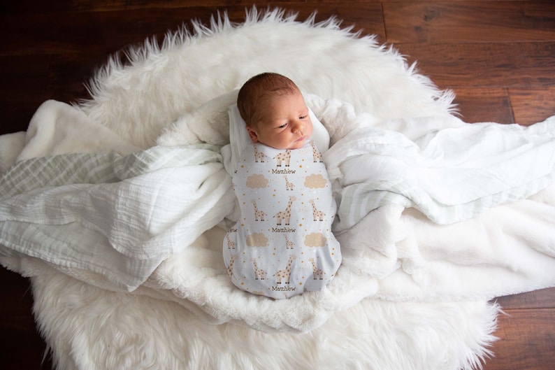 May include: A white swaddle with a giraffe and star pattern. The swaddle is personalized with the name "Matthew".