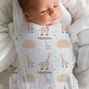May include: A white swaddle blanket with a pattern of brown giraffes, gold stars, and beige clouds. The name "Matthew" is printed three times on the blanket.