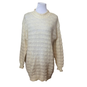May include: A cream-colored long-sleeve sweater featuring a mock neck and a repeating horizontal wavy knit pattern. The garment has ribbed cuffs and a ribbed hem, with a semi-sheer texture throughout the body and sleeves.
